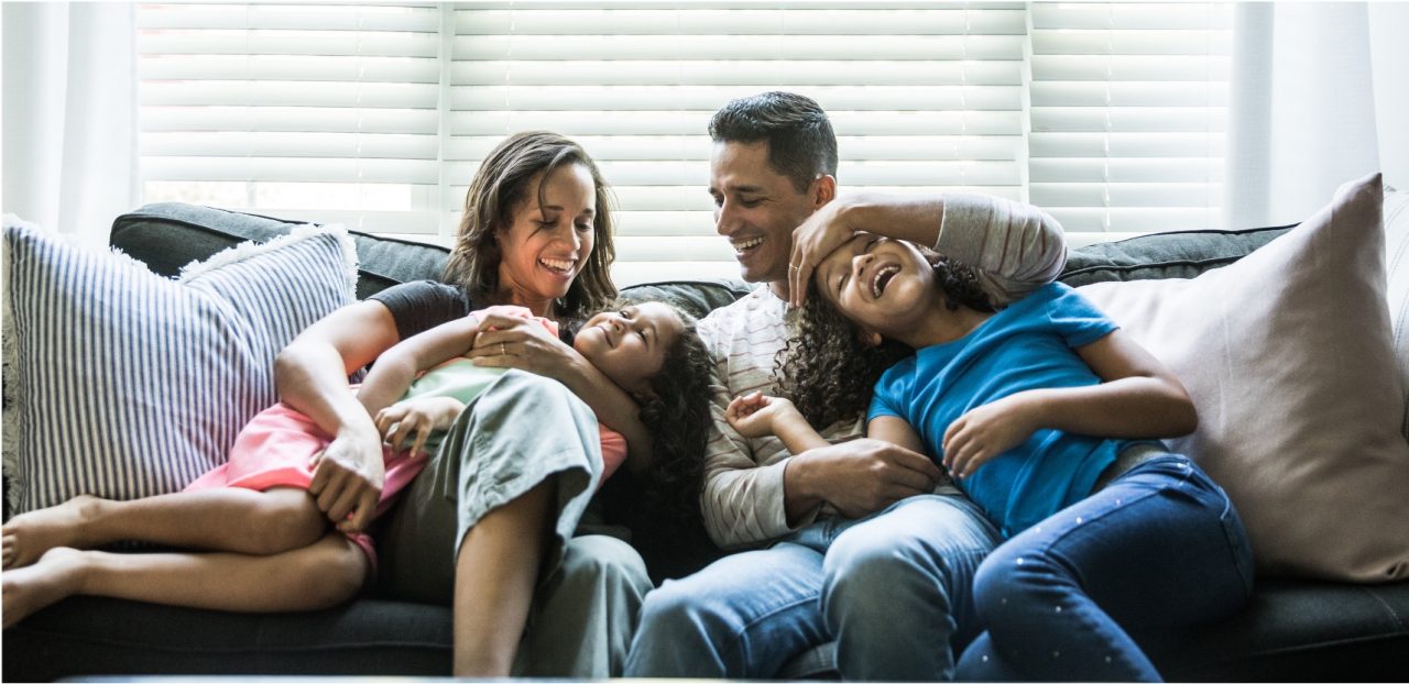 Man and woman sitting on couch playing with their two daughters.